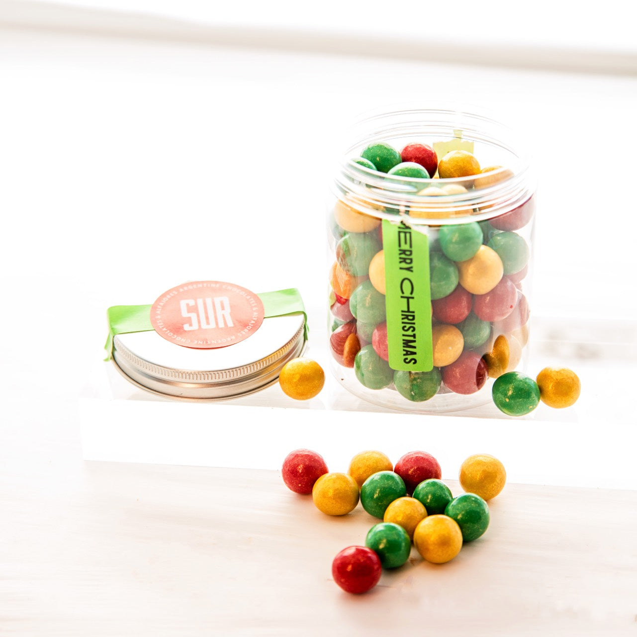 Jar of colorful round crispy chocolates with a 'Merry Christmas' tag on a white background
